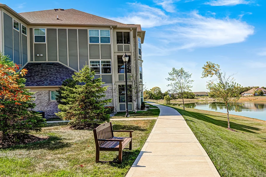 A view of an apartment building and bench looking out over a retention pond at Harmony Apartments